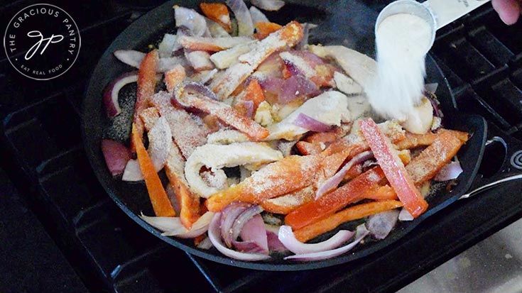 Spices being added to the chicken and vegetables in a skillet.