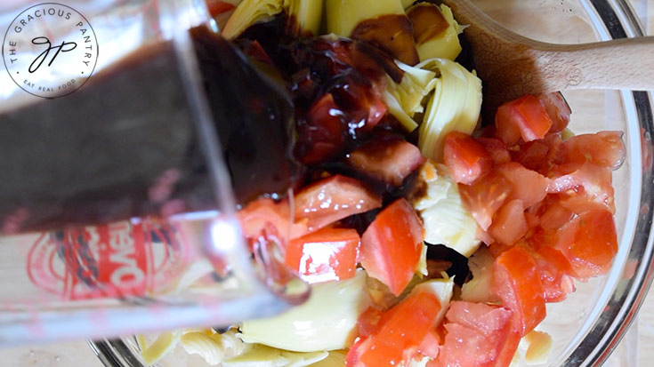 Pouring oil over the pasta salad contents of a mixing bowl.