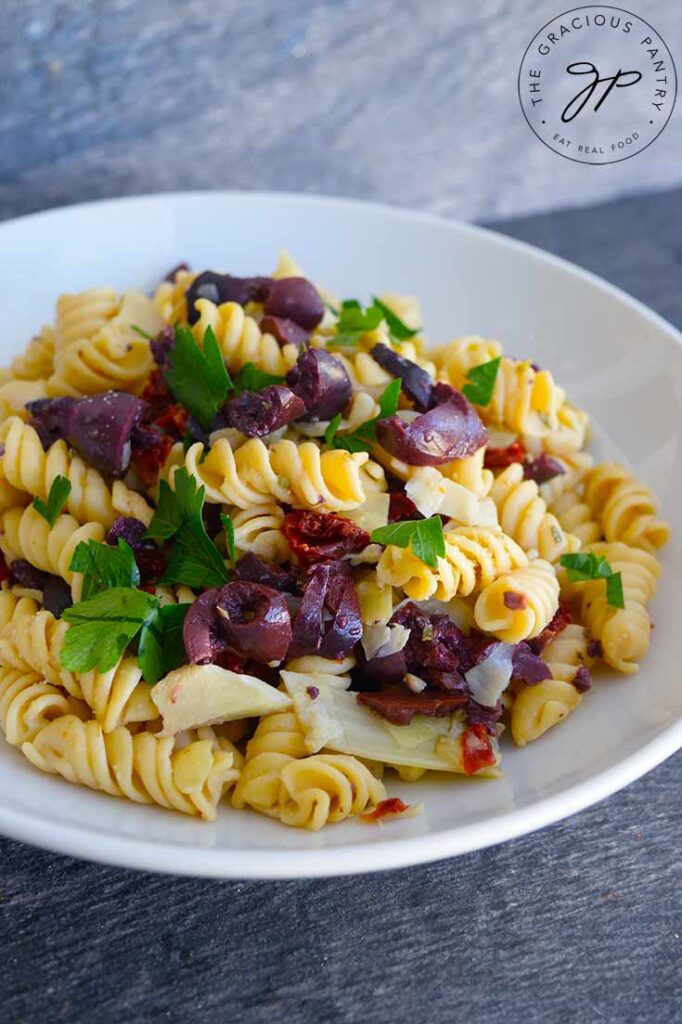 Greek pasta salad with kalamata olives and dried tomatoes in a white bowl.
