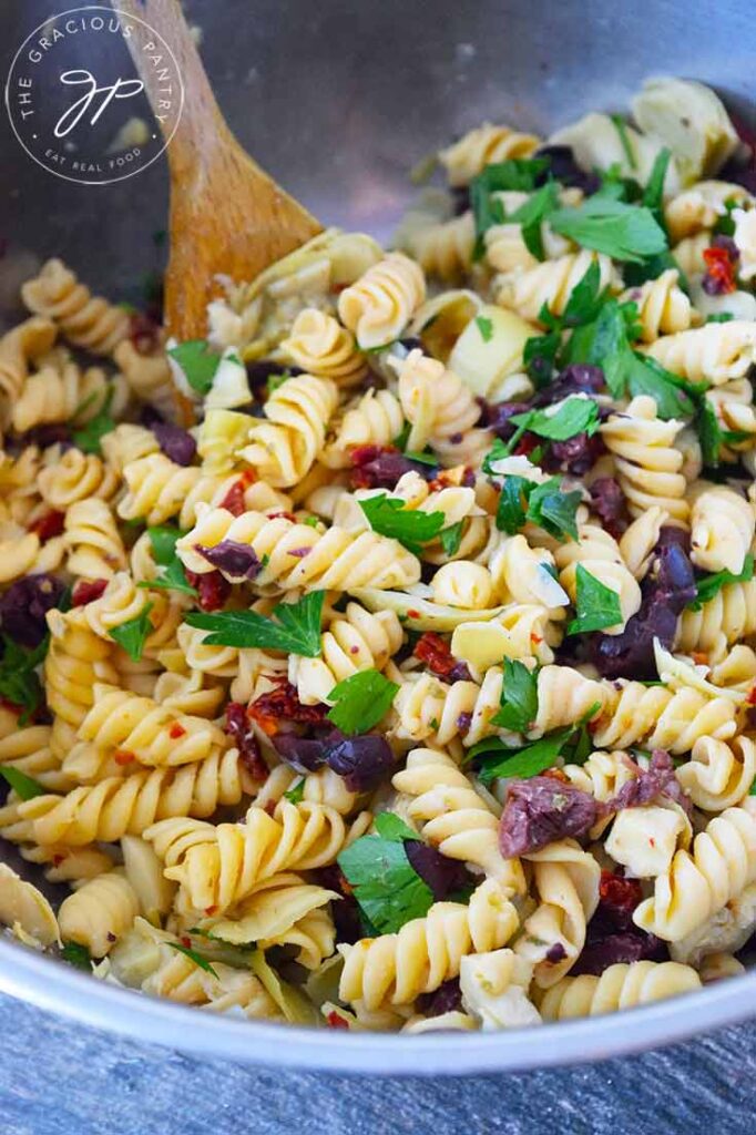 Greek pasta salad in a stainless steel mixing bowl.