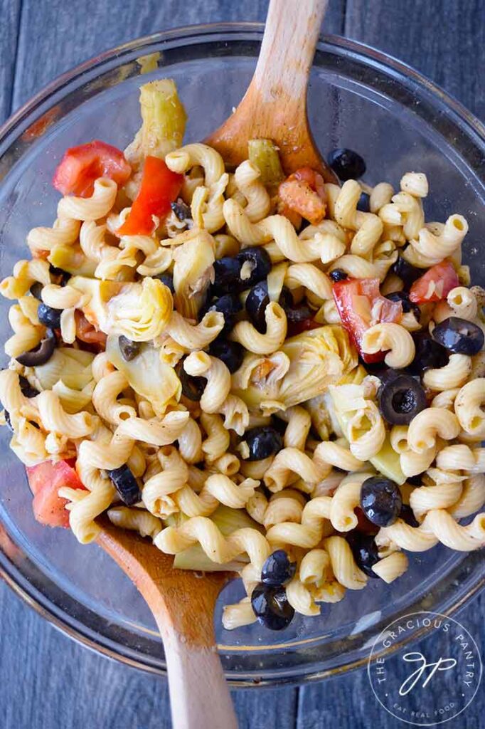 An overhead view looking down into a glass mixing bowl filled with greek pasta salad.