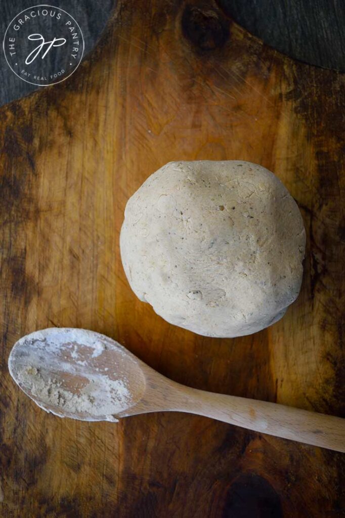 An overhead view looking down on a ball of oat flour pizza crust dough. A used wooden spoon rests next to it with flour and dough on it.