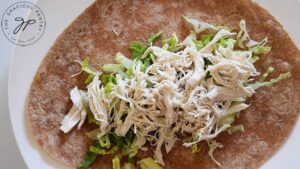 Shredded chicken spread out over lettuce on a whole wheat tortilla.