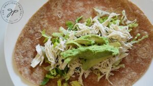 Avocado laying on top of shredded chicken and lettuce on a whole wheat tortilla.