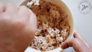 Tuna salad being mixed in a white mixing bowl.