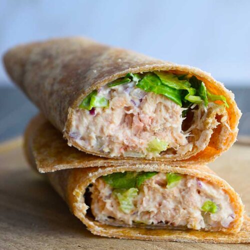 An angled view of a tuna wrap, cut in half and stacked up on a cutting board.