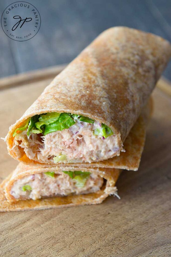 An overhead view of a tuna wrap, cut in half and stacked up on a cutting board.