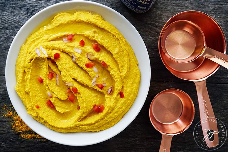 Just finished and garnished Turmeric Hummus served in a white bowl.