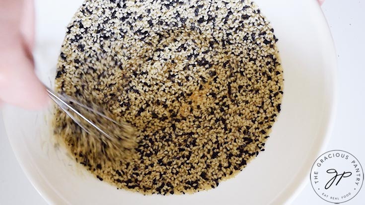 The Everything Bagel Seasoning ingredients being stirred together in a small, white mixing bowl.