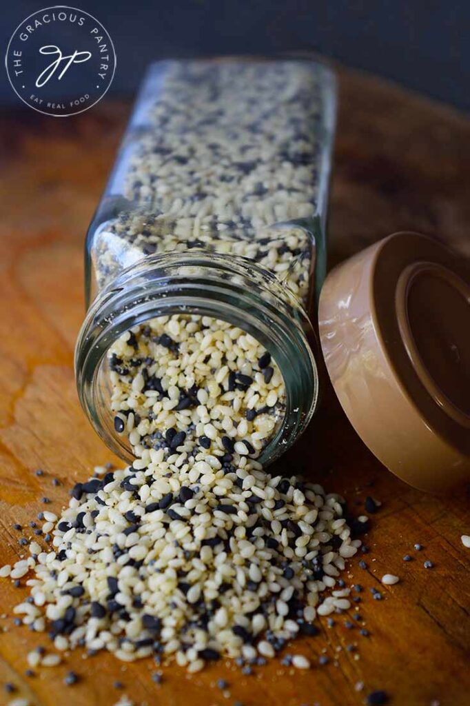 A head on view of a tipped over spice jar with Everything Bagel Seasoning spilling out onto a wooden surface.