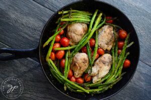 A black, cast iron skillet holds this just-cooked, Oven-Baked Chicken Thighs Recipe With Veggies