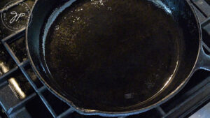 A cast iron skillet, just oiled, sits on a stovetop.