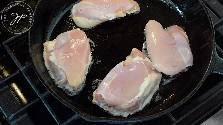 Raw chicken thighs cooking in a black, cast iron skillet.