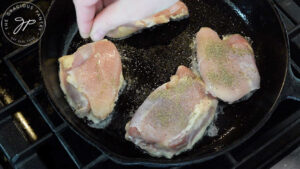 Seasoning chicken thighs in a cast iron skillet.