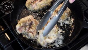 Turning chicken thighs in a cast iron skillet to season both sides.
