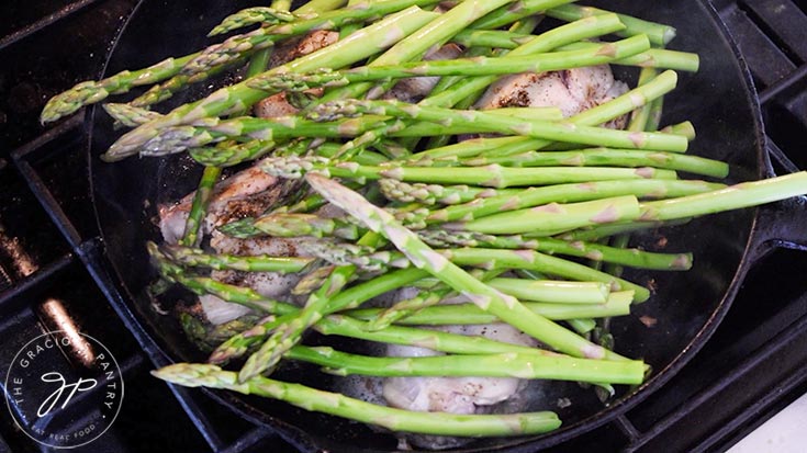 Asparagus laid across thicken thighs in a cast iron skillet.