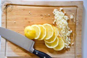 Lemon slices and minced garlic lay on a cutting board. A knife rests to the side.