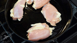 Four raw chicken thighs sitting in an oiled cast iron skillet.
