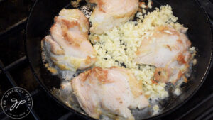 Garlic added to a skillet of chicken thighs.