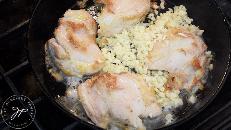 Garlic added to a skillet of chicken thighs.