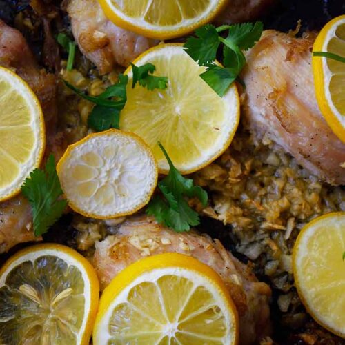 An up close shot of baked chicken thighs topped with lemon slices and minced garlic.