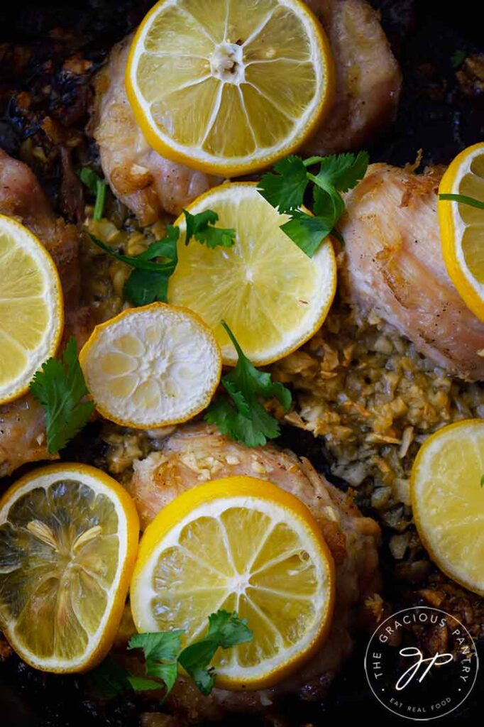 An up close shot of baked chicken thighs topped with lemon slices and minced garlic.