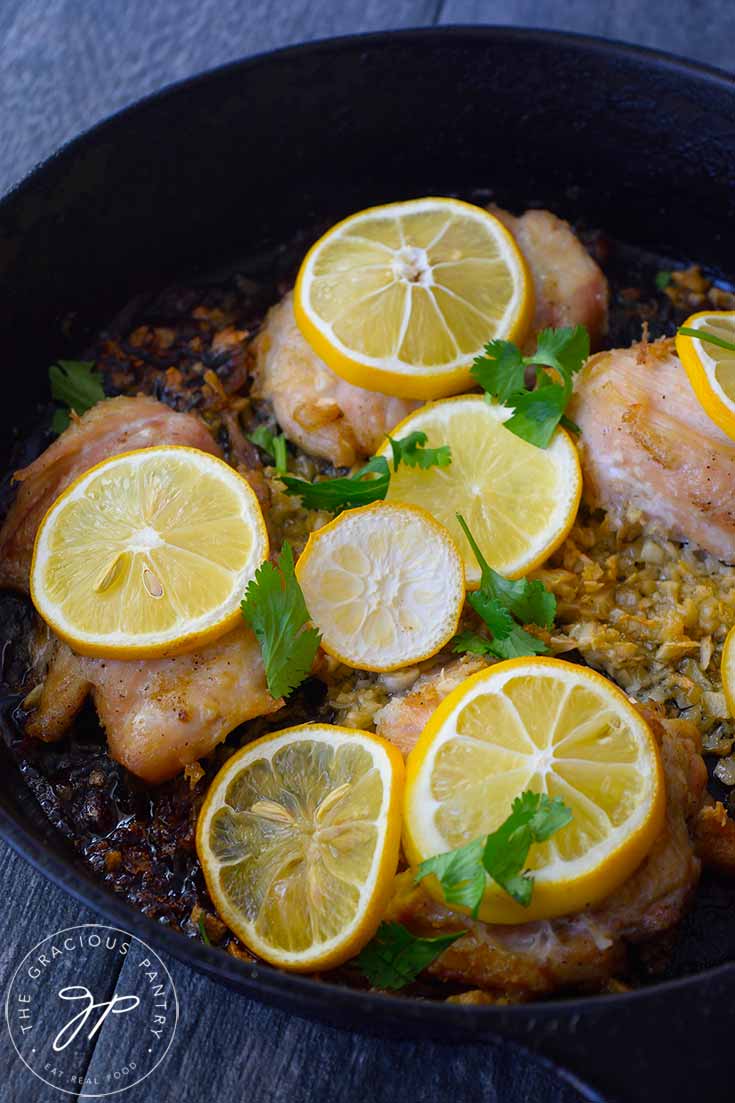 Chicken thighs topped with lemon slices, sit in a bed of mince, roasted garlic in a cast iron skillet.
