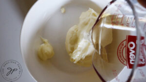 Water being poured into a small white bowl with mayonnaise in it.