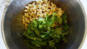 Chopped lettuce added to cooked pasta in a large mixing bowl.