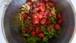 Halved, grape tomatoes added to chopped bacon, lettuce and pasta in a large mixing bowl.