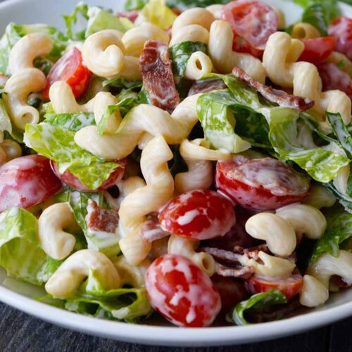 A side view of a white bowl filled with BLT Pasta Salad.