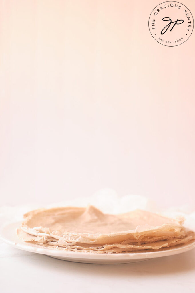 A stack of just-made crepes sit on a white plate.