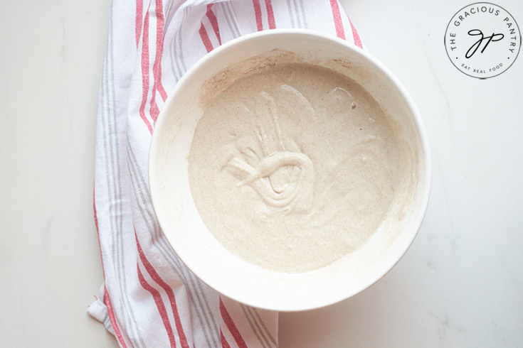 Buckwheat Waffle batter in a white bowl, sitting on a red and white striped dish towel.