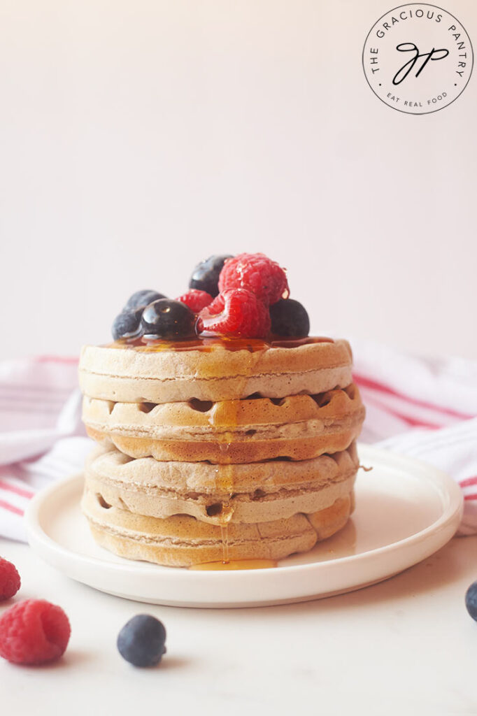 A stack of buckwheat waffles on a white plate, topped with blueberries and raspberries.