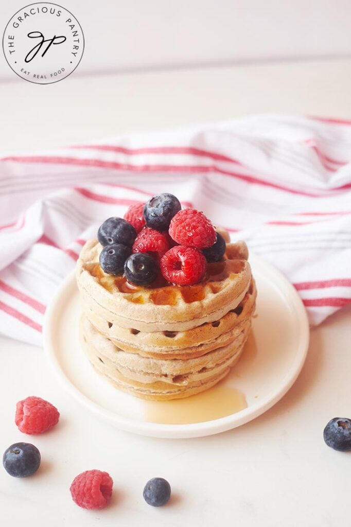 A stack of buckwheat waffles sits on a white table with a dishcloth behind it.