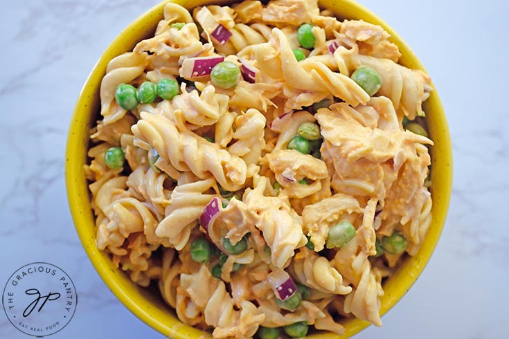 A yellow bowl sits filled with buffalo chicken pasta salad on a white, marble background.