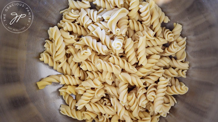 A stainless steel mixing bowl holds cooked rotini pasta.