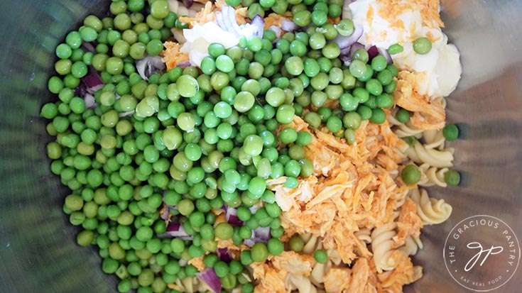Green peas, may, shredded chicken and cooked pasta in a mixing bowl.