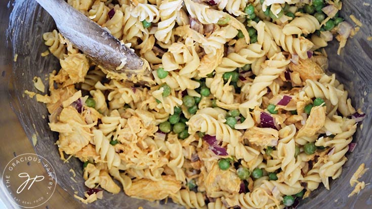 Buffalo chicken pasta salad mixed together and sitting in a mixing bowl with a wooden spoon.