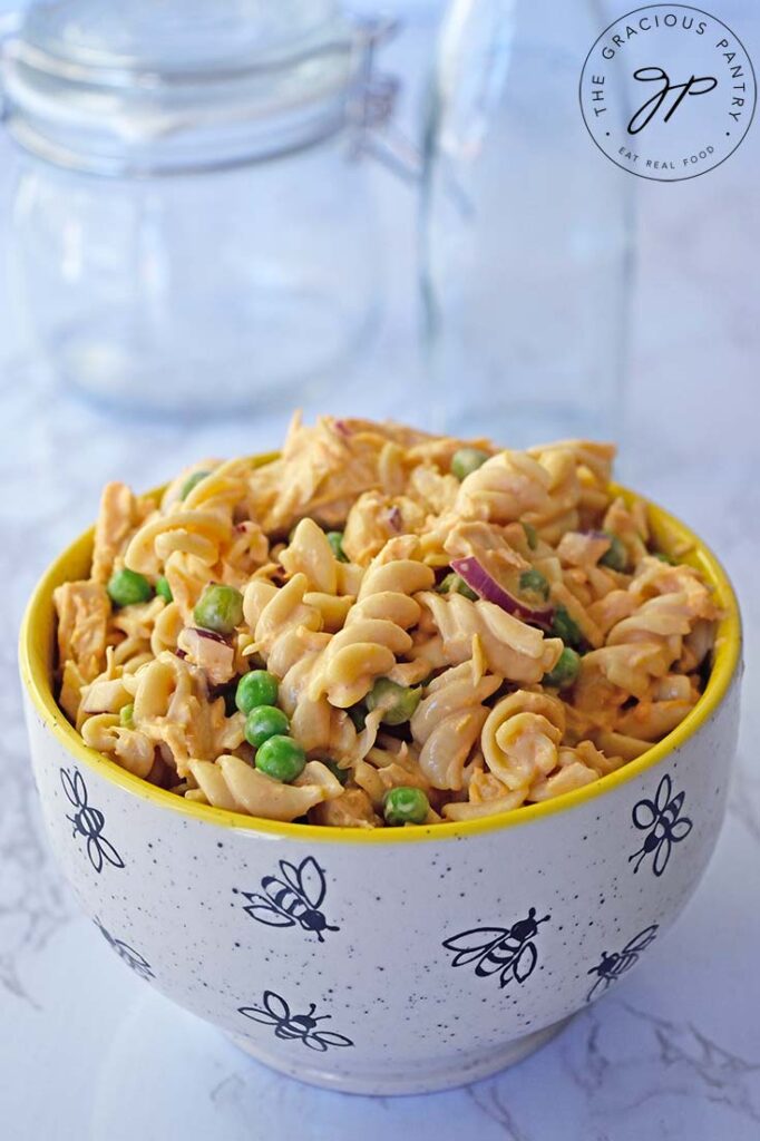 Buffalo chicken pasta salad fills a small bowl which sits on a white, marble surface.