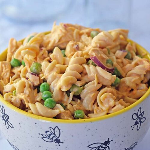 A close up of a bowl filled with buffalo chicken pasta salad sitting on a white, marble surface.