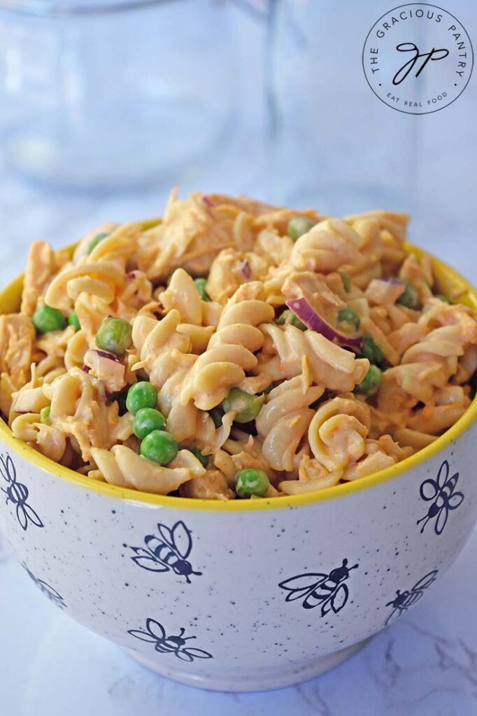 A close up of a bowl filled with buffalo chicken pasta salad sitting on a white, marble surface.