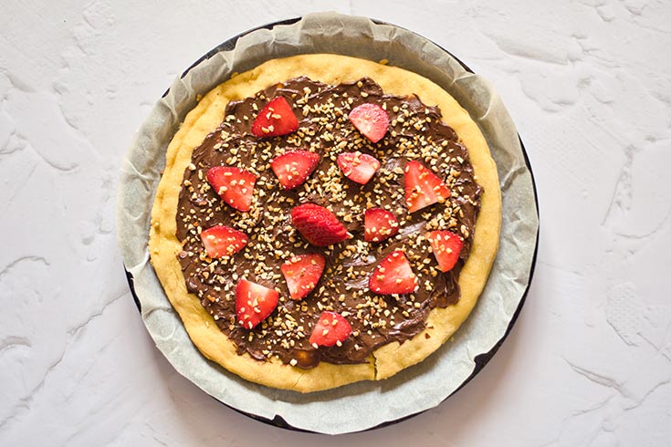 The chocolate pizza topped with strawberries and chopped hazelnuts.