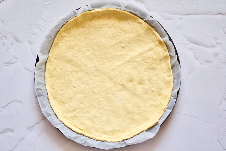 Pizza crust rolled out an placed on a round pizza pan.