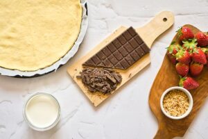 Chopped chocolate sitting on a cutting board with other ingredients for this chocolate pizza surrounding it.