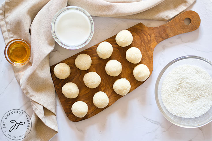 Ungarnished coconut balls in a row on a cutting board.