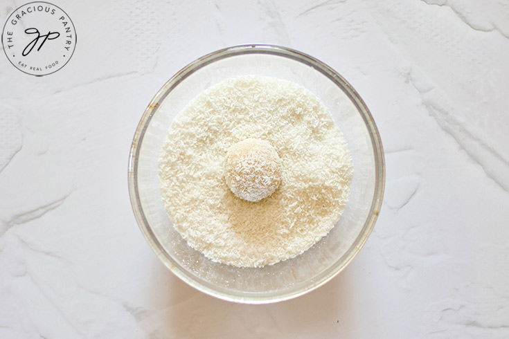 A single coconut ball sitting in a bowl of shredded coconut.