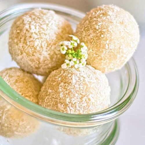 Four coconut balls in a glass container and garnished with some small white flowers.