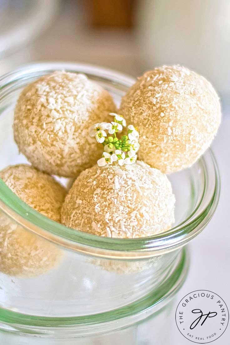 Four coconut balls in a glass container and garnished with some small white flowers.