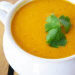 A white crock filled with Curried Sweet Potato Soup and garnished with fresh cilantro.